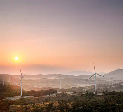 Wind Turbines generating renewable electricity on top of rolling hills at sunrise. 